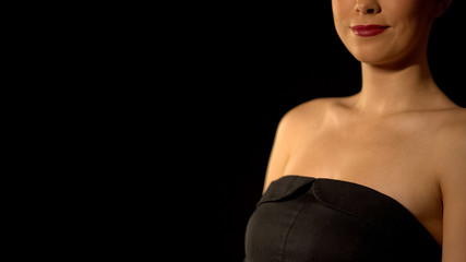Elegant woman in black dress standing against black background, beauty concept