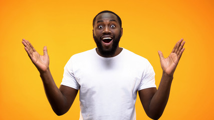 Excited black male looking camera on bright background, surprise reaction, news