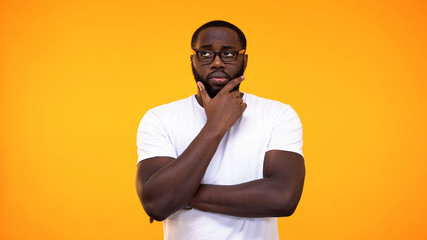 Smart young black student in glasses thinking about answer, yellow background