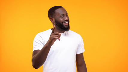 Smug afro-american man pointing finger camera and smiling yellow background