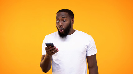 Surprised afro-american guy looking at phone screen, lottery winner, betting app