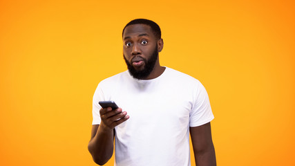 Stunned young man holding smartphone in hand, banking application, cash back