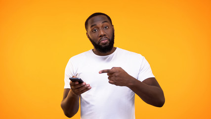 Young afro-american man pointing at smartphone in hand, recommending application