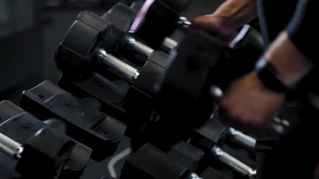 Athlete takes dumbbells in hand, view of gym equipment, close up.