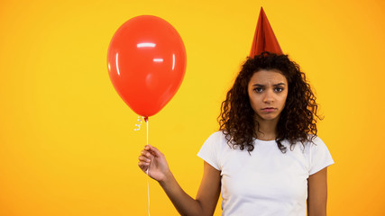 Sad young female holding red balloon, upset and lonely on birthday celebration
