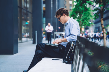Side view of male entrepreneur using portable pc for making banking via application online using 4G internet while sitting at city area in downtown, intelligent man using tablet for payment money