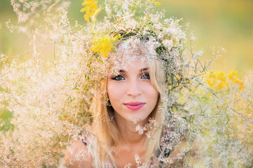 beautiful happy young lady in a wreath of summer flowers on nature
