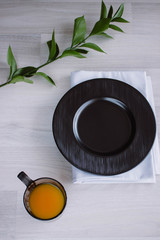Black plate on white wooden background. With plant and napkin,top view. Empty plate for serving with orange juice
