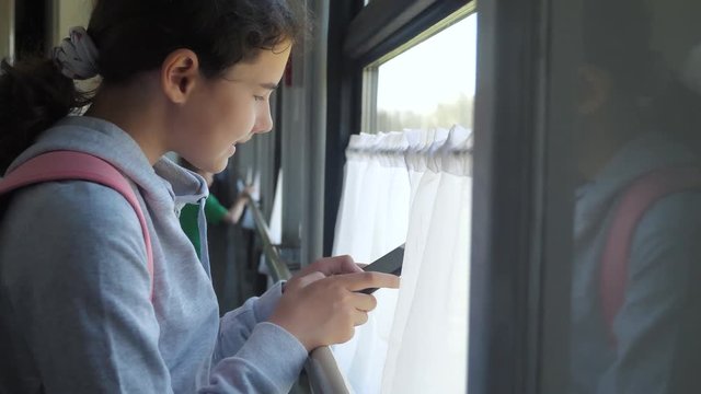 girl teenager traveler with backpack stands by the window of the train car with a smartphone. travel transportation railroad concept. the girl lifestyle in the train at the window corresponds the girl