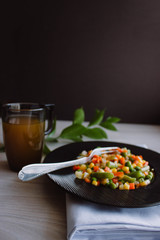 Frozen fried vegetables on black plate. Vegan breakfast with juice. Vegetables food mix on white wooden background with plant.