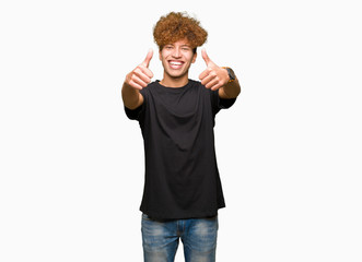 Fototapeta premium Young handsome man with afro hair wearing black t-shirt approving doing positive gesture with hand, thumbs up smiling and happy for success. Looking at the camera, winner gesture.