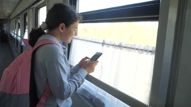 girl teenager traveler with backpack stands by the window of the train lifestyle car with a smartphone. travel transportation railroad concept. the girl in the train at the window corresponds the girl