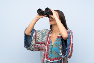 Young woman over isolated blue wall with black binoculars