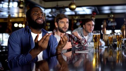 Extremely emotional black supporter watching game with friends, relaxing in bar