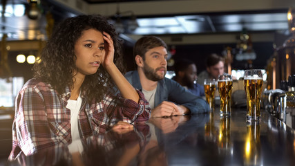 Unhappy pretty biracial lady disappointed about team losing game, leisure in bar