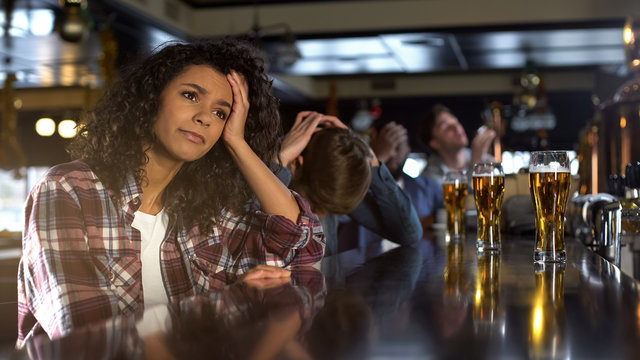 Disappointed biracial female with male friends watching sport game in bar, loss