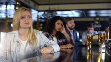 Pretty blond girl upset about losing game, watching sports with friends in pub