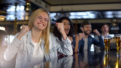 Pretty woman celebrating victory with friends watching sports in pub, broadcast