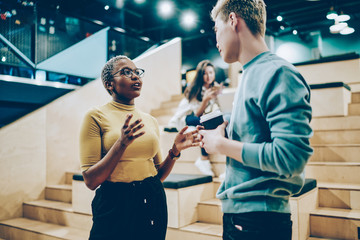 Young african american woman explaining information to male colleague standing on break in coworking office, multiracial students in casual wear communicating on free time share ideas for project.
