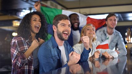 Cheerful Italian fans holding flag celebrating winning match, happy time in bar