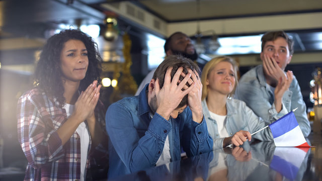 Deeply unhappy french football fans with flag, watching sports program in bar