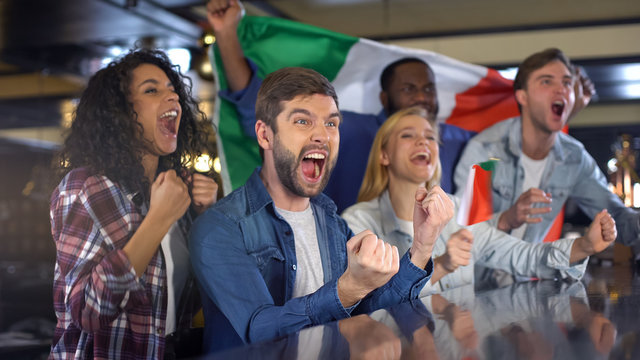 Italian fans with flag celebrating winning game, enjoying championship in bar