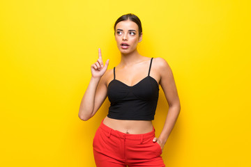 Young woman over isolated yellow background thinking an idea pointing the finger up