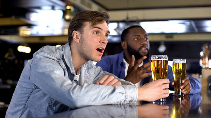 Nervous male friends attentively watching sport match drinking beer, support