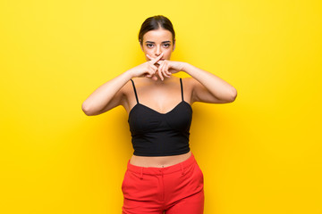 Young woman over isolated yellow background showing a sign of silence gesture