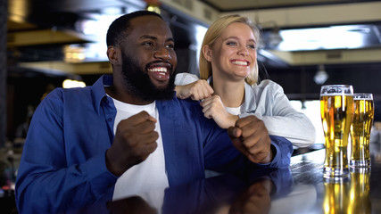 Young biracial couple rooting favorite sport team in bar, watching match online