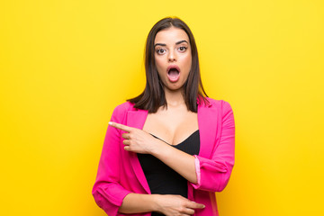 Young woman over isolated yellow background surprised and pointing side