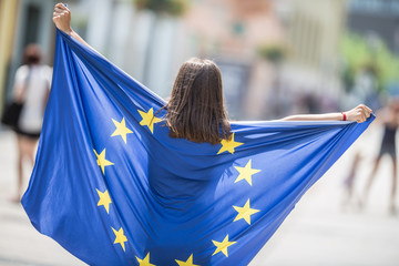 Cute happy young girl with the flag of the European Union in the streets somewhere in europe - obrazy, fototapety, plakaty