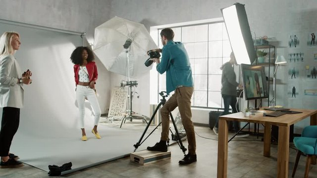 Backstage of the Photo Shoot: Make-up Artist Applies Makeup on Beautiful Black Model, in a Moment Photographer Starts Taking Photos with Professional Camera. Fashion Magazine Photoshoot