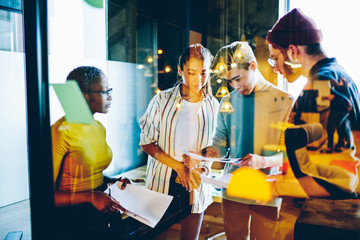 Skilled young multiracial students checking information from paper cooperate on coursework project,...
