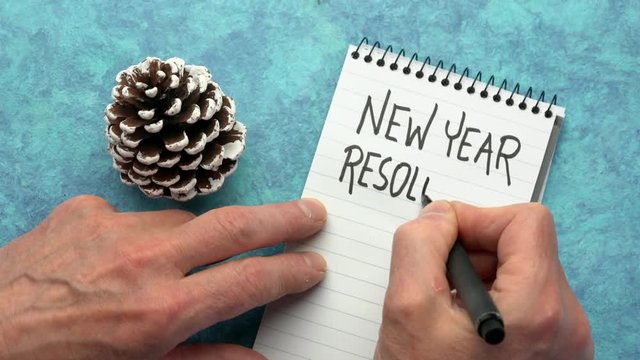 New Year resolutions - man hand writing in a notebook, overhead view