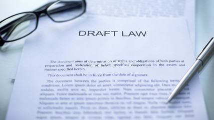 Draft law lying on table, pen and eyeglasses on official document, business