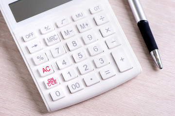 White calculator and pen on bright wooden table, analytics and statistics of financial profit, investment risk concept, copy space, macro, close up