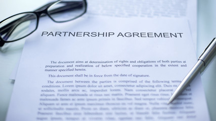 Partnership agreement lying on table, pen and eyeglasses on official document