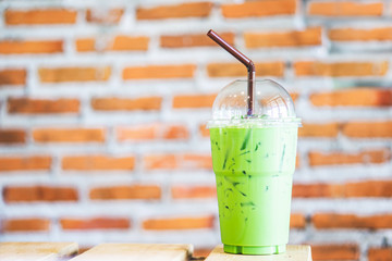 iced green tea latte with milk in plastic cup on wooden table at cafe 