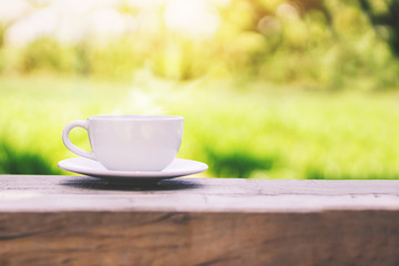 hot coffee cup on wooden table over nature green background with morning sunlight 
