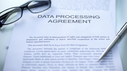 Data processing agreement lying on table, pen and eyeglasses on document, close - Powered by Adobe