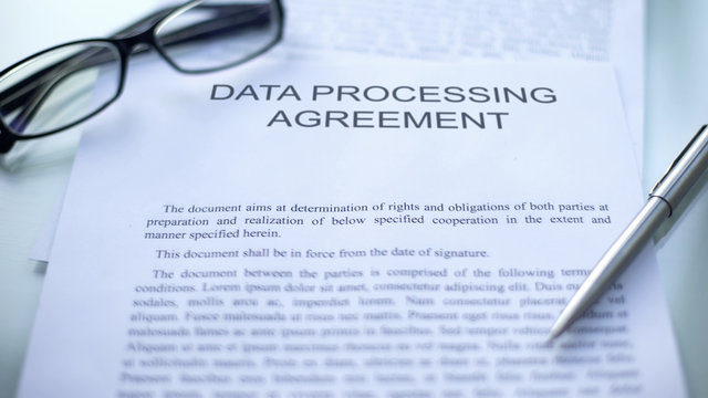 Data processing agreement lying on table, pen and eyeglasses on document, close