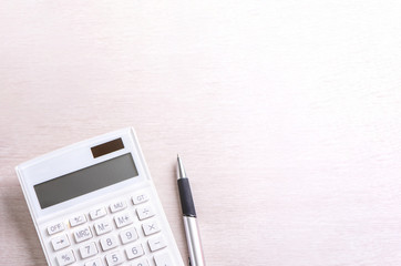 White calculator and pen on bright wooden table, analytics and statistics of financial profit, investment risk concept, copy space, top view flat lay