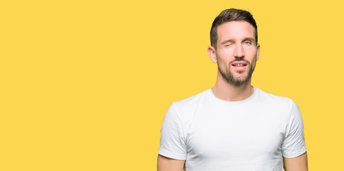 Handsome man wearing casual white t-shirt winking looking at the camera with sexy expression, cheerful and happy face.