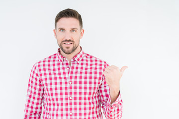 Obraz premium Young handsome man wearing shirt over isolated background smiling with happy face looking and pointing to the side with thumb up.
