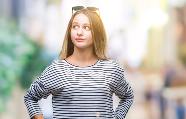 Young beautiful blonde woman wearing sunglasses over isolated background smiling looking side and staring away thinking.