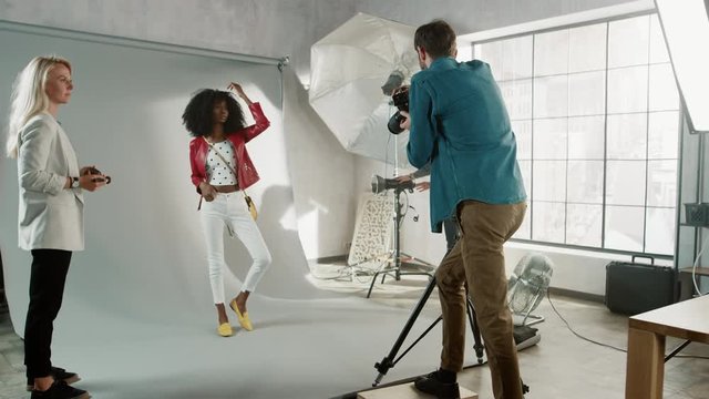 Backstage of the Photo Shoot: Make-up Artist Applies Makeup on Beautiful Black Model, in a Moment Photographer Starts Taking Photos with Professional Camera. Fashion Magazine Photoshoot