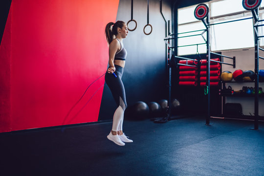 Side View Of Active Hipster Girl In Sport Closing Skipping Rope During Cardio Training In Gym, Attractive Caucasian Fitness Woman Using Equipment For Jumping And Slimming In Pilates Studio