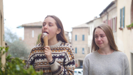 Two young women walking on the town and one of them eat icecream