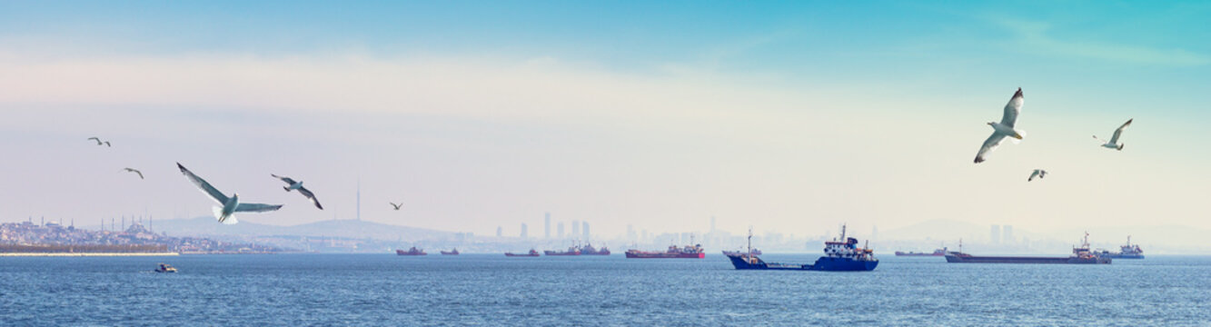 Marine navigation and sea traffic at the Bosphorus Strait. Wide panorama of Istanbul with silhouettes of freight ships and fishing vessels on a skyline.